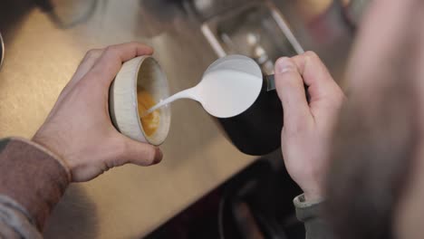 vertical, hip man pours cream into coffee cup to practice making latte art