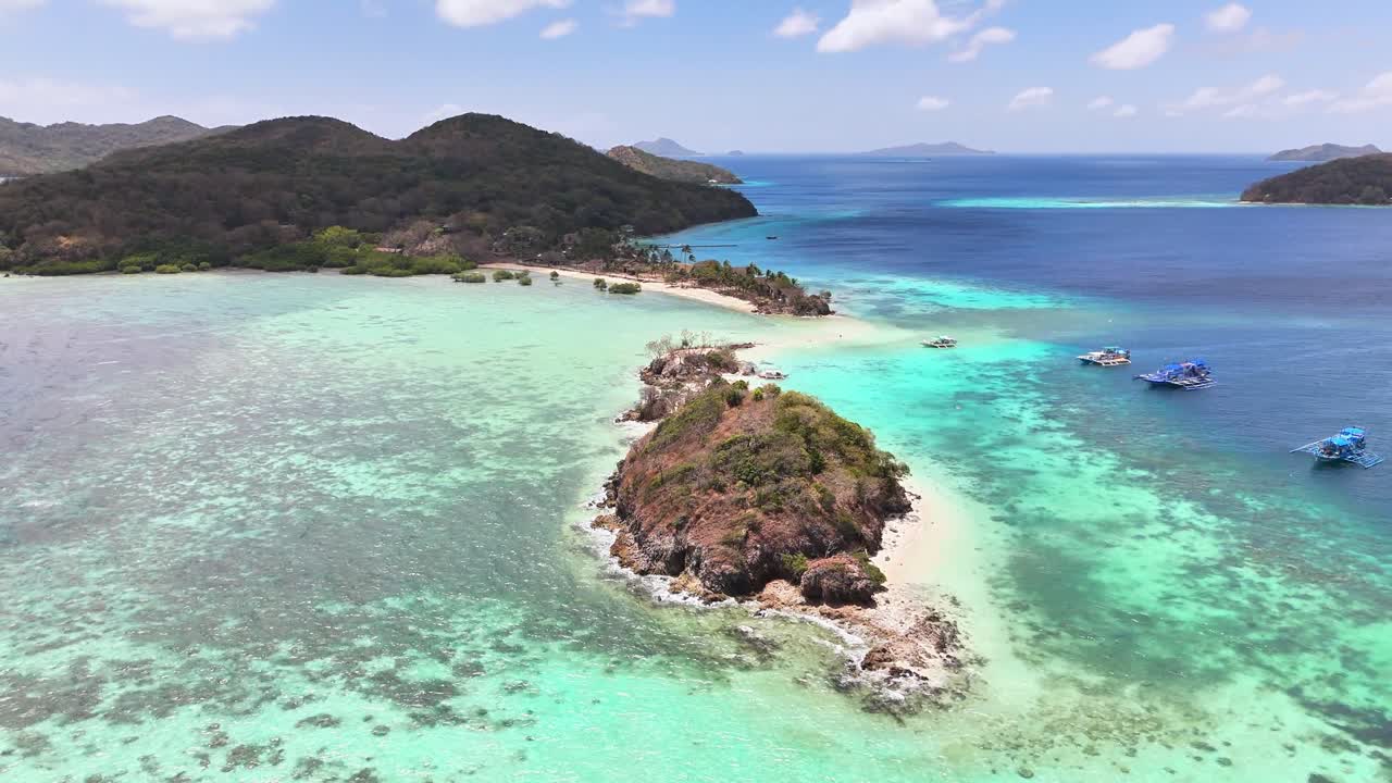 Aerial view of Bulog Dos Island in the Philippines with vivid turquoise waters, a connecting sandbar, coral reefs, forested islets, and anchored boats under bright tropical skies