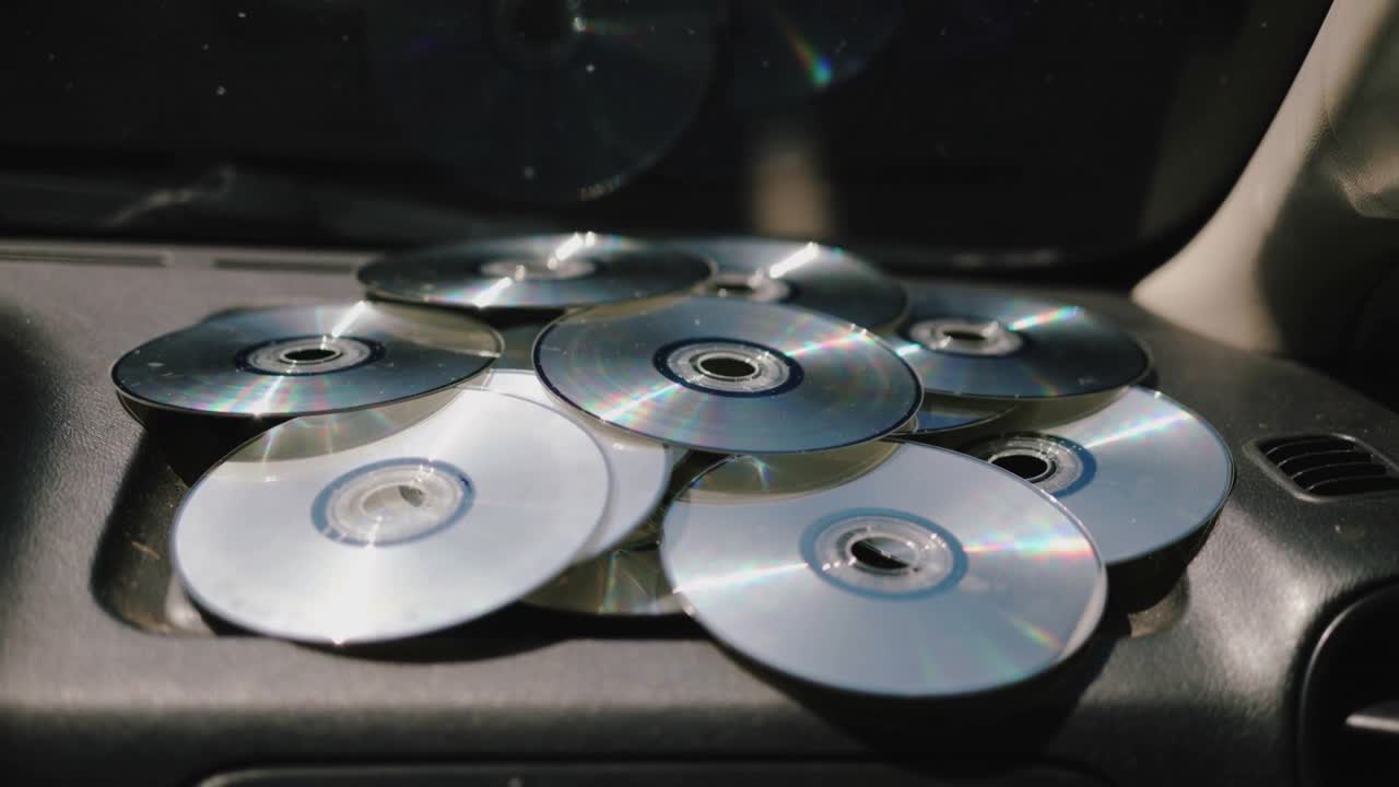 Skiftende lys kaster regnbueglimt på ni CD'er på instrumentbrættet nær udluftningen med et let kameraskift