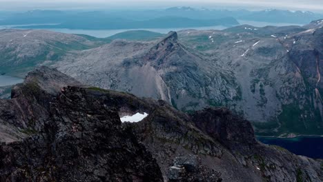 Vista-Aérea-De-La-Montaña-Kvaenan-Con-Un-Acantilado-Irregular-Y-La-Isla-Pico-Fin-Senja,-Noruega