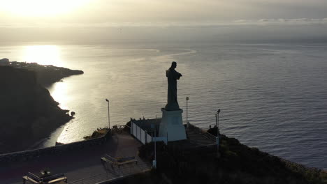 Cristo Rei aka Christ the King Statue. Aerial View of Madeira Island Clifftop Monument Above Atlantic Ocean Coastline and Horizon, Portugal - Drone Shot