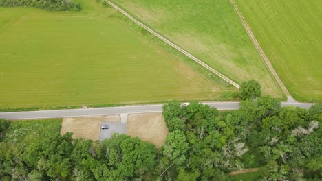 Ein-Roter-5-Tonner,-Der-Auf-Einer-Leeren,-Kurvigen-Straße-Zwischen-üppigen-Grünen-Wiesen-Und-Dichten-Laubbäumen-Fährt