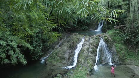 Acending-aerial-slow-motion-view-of-a-young-east-indian-woman-taking-a-selfie-at-a-waterfall