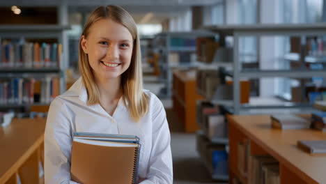 young woman smiling in a library holding books