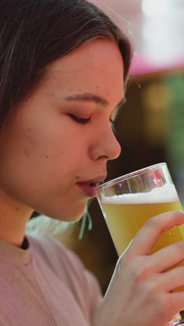 una mujer bebe cerveza en un pub de primer plano. una joven de cabello oscuro toma un sorbo de cerveza fresca descansando sola en un bar. una invitada bonita con una bebida alcohólica