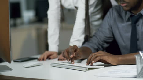 black man in glasses and woman sitting at office desk and viewing something on computer when working late in the evening 1