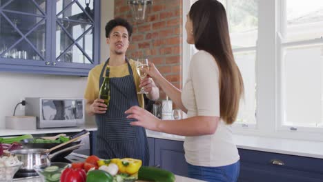 happy biracial couple cooking together and drinking wine in kitchen