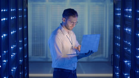 male server engineer in data center. it engineer inspecting a secure server cabinet using modern technology laptop coworking in data center.