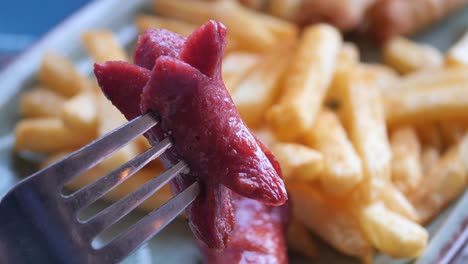 primer plano de una salchicha a la parrilla en un tenedor con papas fritas