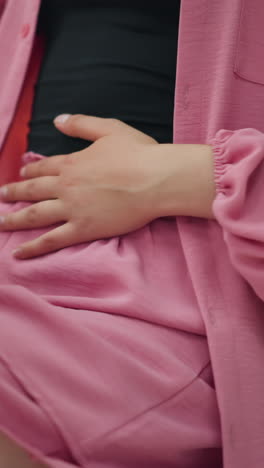 mujer con una camiseta negra bajo un vestido rosado frotando suavemente el estómago con la mano derecha, la otra mano colocada en la mesa después de una comida, el fondo presenta una luz borrosa roja