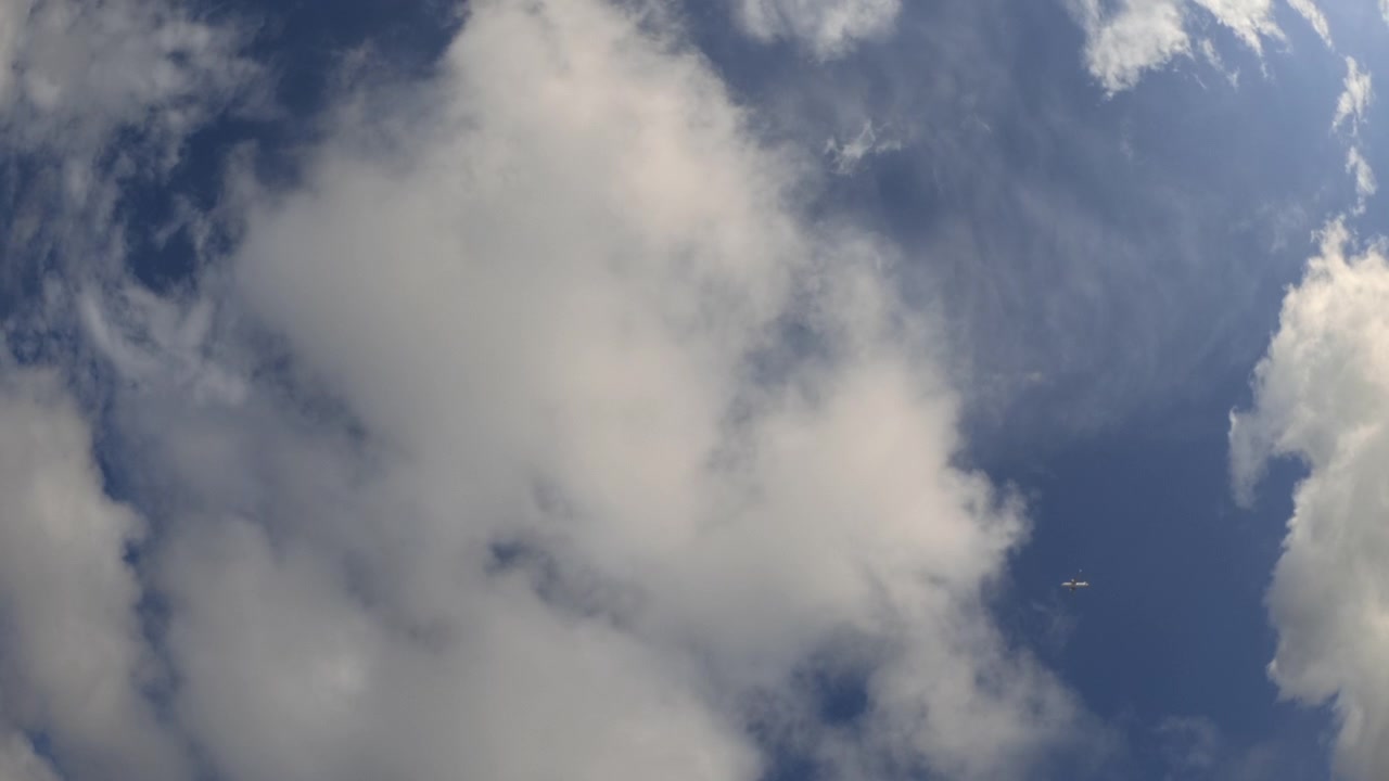 Wide view of an airplane flying across a blue sky with clouds