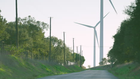large wind turbines rise in distance near rural countryside road