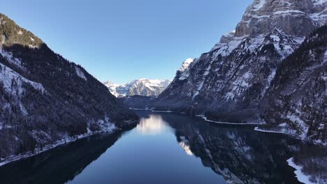 Aerial Klöntalersee reflecting snowy Alps in Klöntal, Switzerland, serene winter landscape