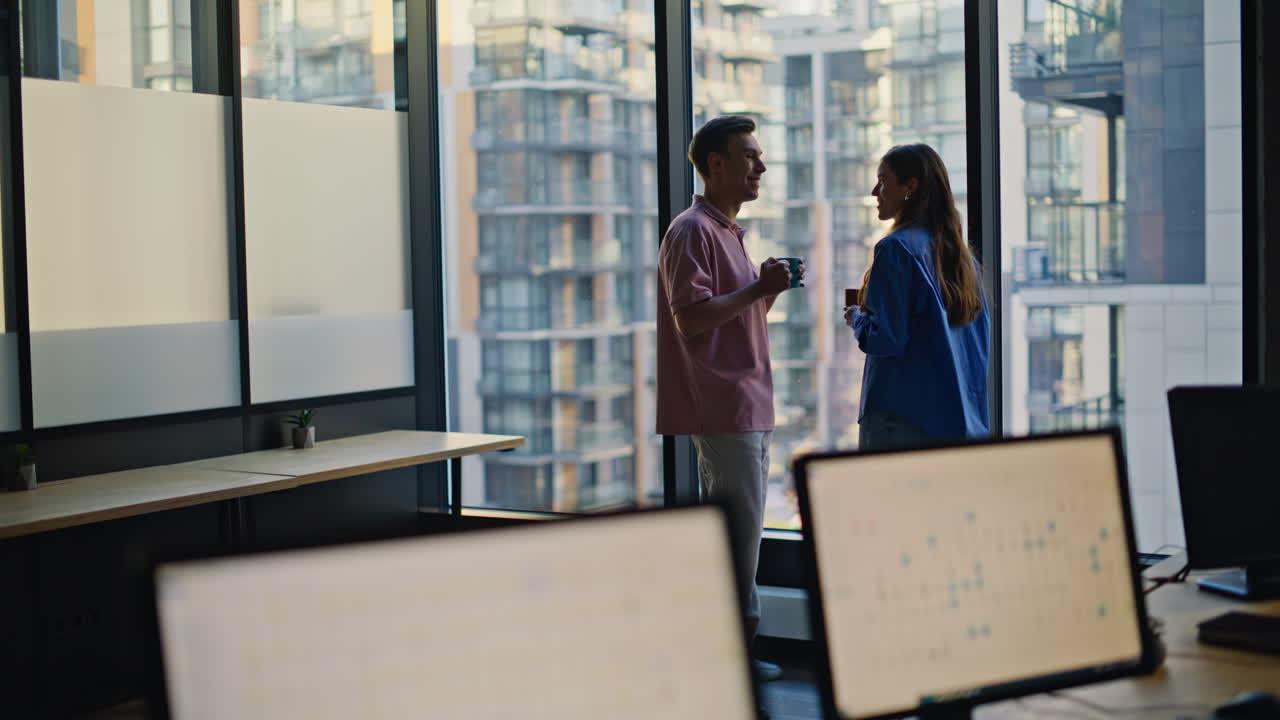 Office colleagues sharing coffee standing together at panoramic building window