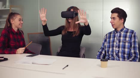 Handsome-woman-tries-app-for-VR-helmet-virtual-reality-glasses-while-her-friends-and-colleagues-supporting-her-in-a-modern-office.-Team-of-workers-using-innovative-future-technology-through-Vr-headset