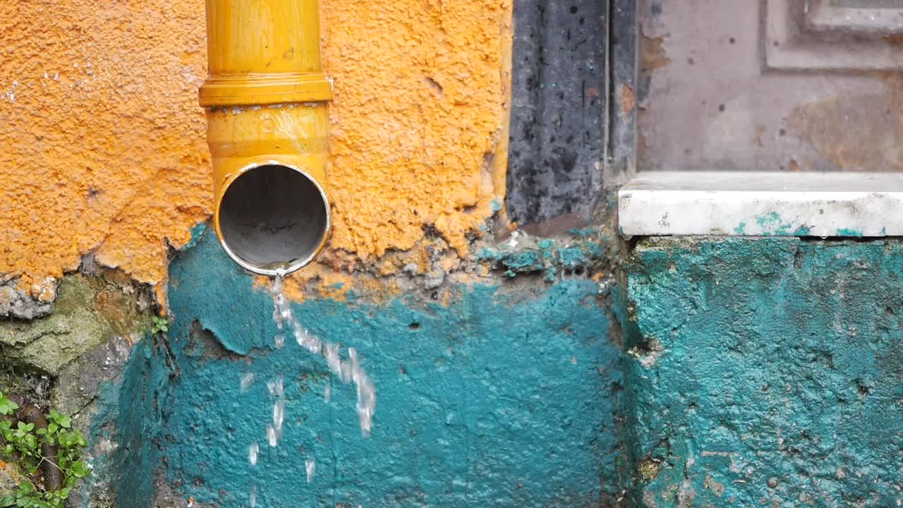 Water dripping from a yellow gutter on a multi-colored building wall