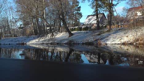 magnífico ángulo bajo lentamente panorámica imágenes de un río oscuro agua en laagri pääsküla durante el invierno donde los patos mallard están nadando y descansando en. el sol está brillando en las orillas nevadas del río, cielo azul