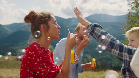 family playing blowing soap bubbles in summer mountains. parents amusing kids.