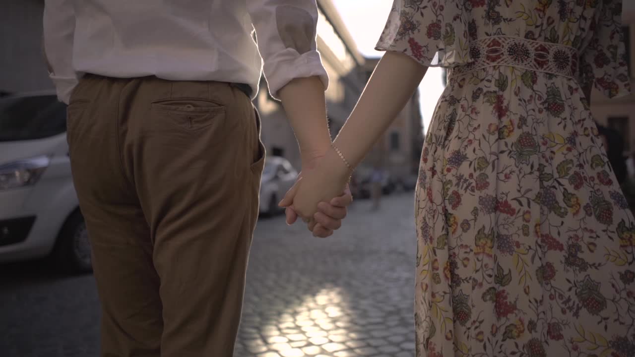 Lovers holding hands and walking forward at sunrise in Rome