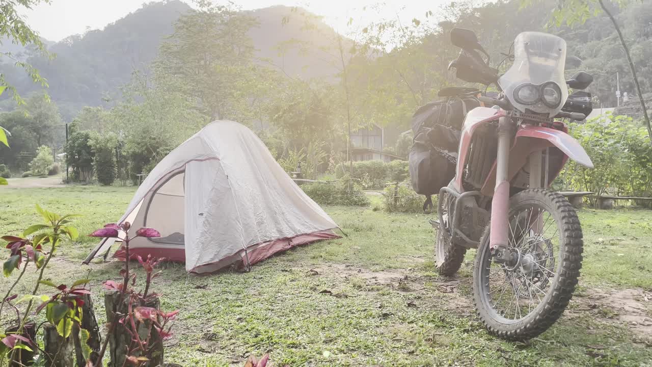 Solo cyclist stops to camp in open field, past lush hills and fog in early morning countryside scene