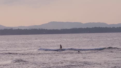 surfer in silhouette riding wave with mountains in background