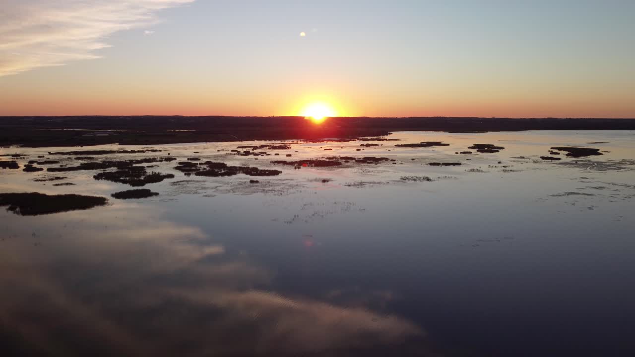 Kran-droneoptagelse ved solnedgang over en sø, vådområder med en flod i baggrunden