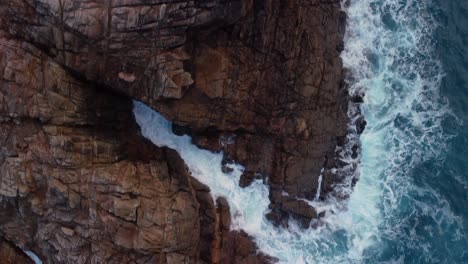 Top-Down-View-Of-Foamy-Waves-Splashing-On-Rugged-Cliffs-In-Arteixo,-Spain---drone-shot