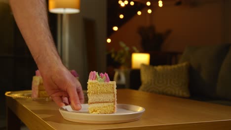 person putting down slice of party celebration cake for birthday decorated with icing on table at home