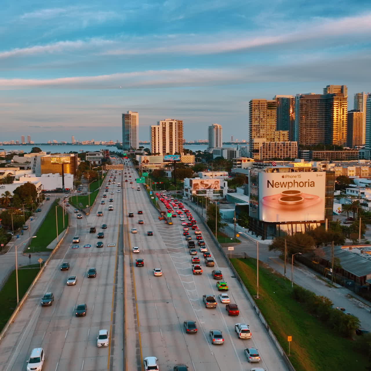 Lots of cars move by the multi-lane highway and stand in the congestion. Drone footage above Miami, Florida at sunset.