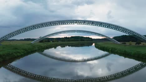 flying under two bridges for gas pipes running across the calm river moravia on the border of slovakia and czechia. aerial sunset footage of two symmetrical gas pipe bridges reflecting in water