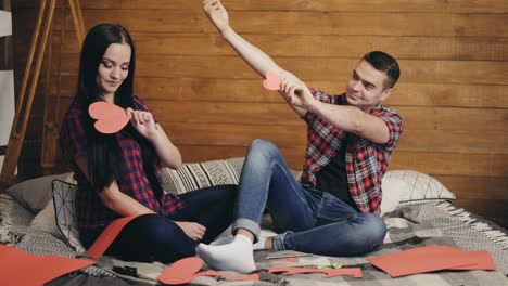 enamored are sitting on the bed and holding red paper hearts in their hands and playing. love story.