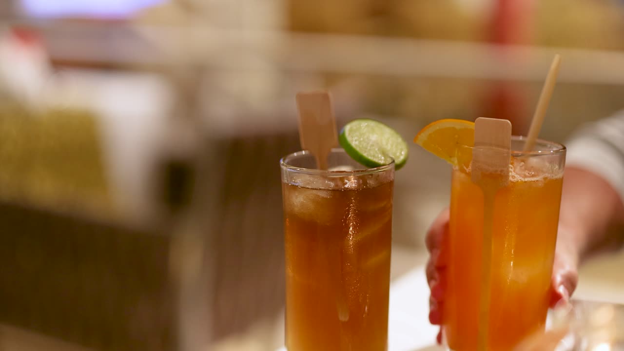 Hand serving colorful cocktails garnished with citrus slices slowly
