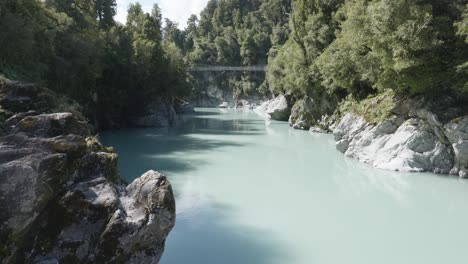 Swingbridge-over-Hokitika-river-flowing-through-Hokitika-Gorge-with-forests-on-a-sunny-summer-day-at-West-Coast,-New-Zealand