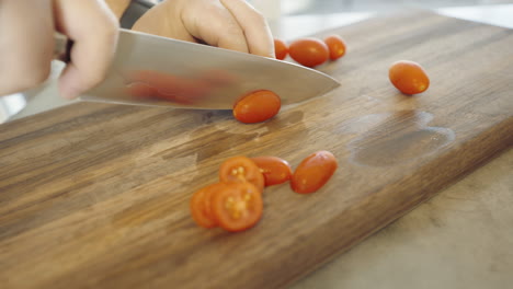 cutting tomatoâ€™s on a wooden cutting board with halved tomatoâ€™s in the foreground