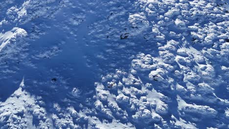 Snow-covered-Bucegi-Mountains-bask-in-sunlight,-shadow-play-on-rugged-terrain,-aerial-perspective