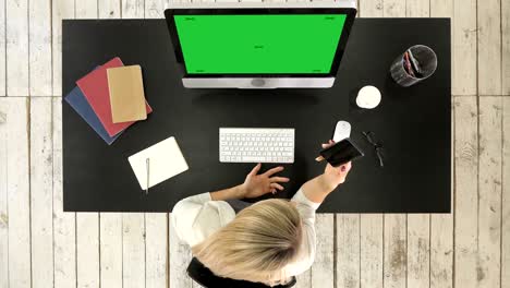 young blonde woman texting message on smartphone on her workstation. green screen mock-up display