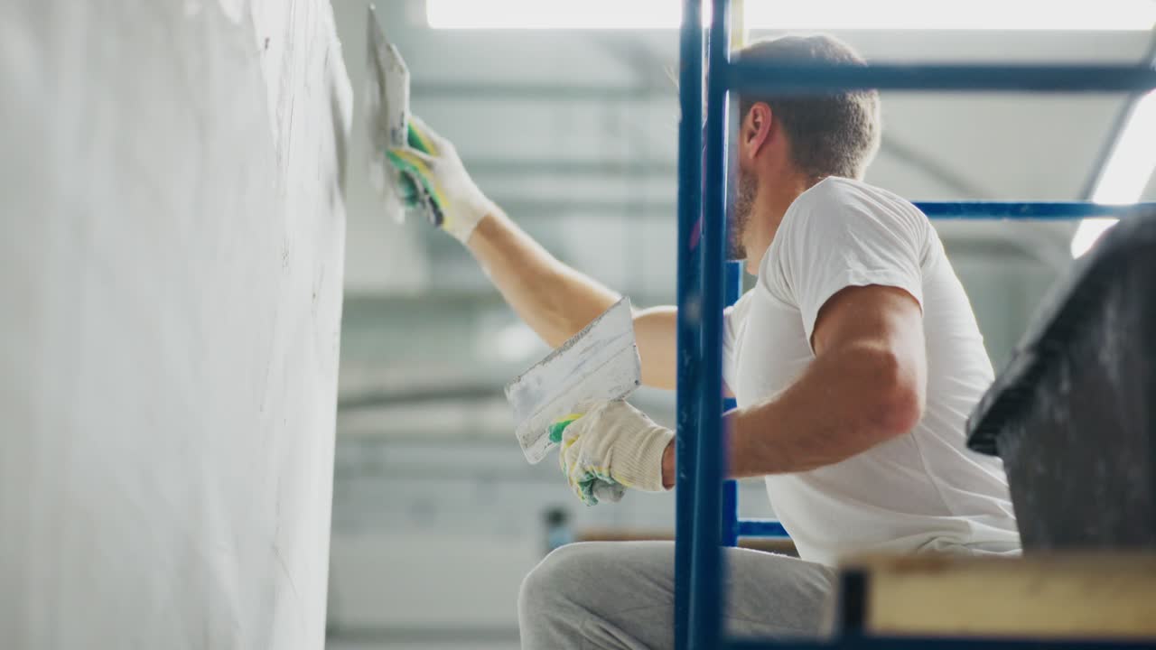 A Focused Worker Skillfully Applies Finishing Touches to a Wall Using a Trowel, Surrounded by Modern Equipment in a Well-Lit Workspace