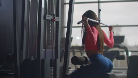 The-young-female-performs-a-personal-training-on-the-muscles-of-the-back.-She-starts-a-barbell-with-an-additional-weight-behind-her-back.