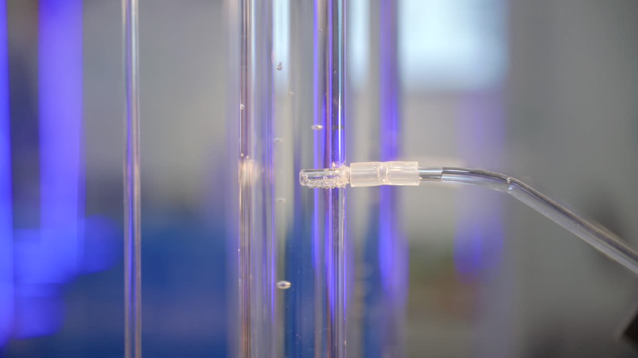 Hydrogen gas is flowing into a glass cylinder filled with water, slow motion, blue futuristic light in a laboratory.