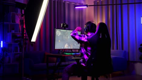 back view of asian boy streamer screaming goal and dancing celebrating winning game over network on personal computer.  live stream video game, desk illuminated by rgb led strip light