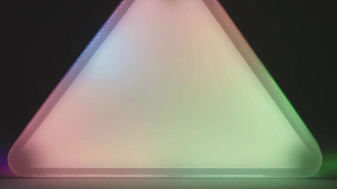 Lampada LED triangolare che cambia tonalità su un tavolo da studio a bassa lucentezza dopo un timer per la luce diffusa di un diffusore satinato.