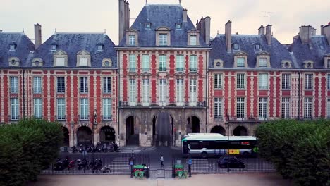 city bus driving on road around pavillon de la reine on place des vosges, paris, france