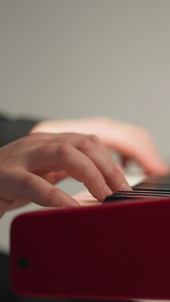 un tecladista con un traje negro se sienta y toca un sampler rojo contra un fondo gris. el enfoque está en las manos tocando el teclado, destacando el rendimiento detallado y hábil