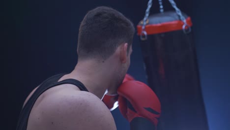 lone boxer punching punching bag in dark gym.