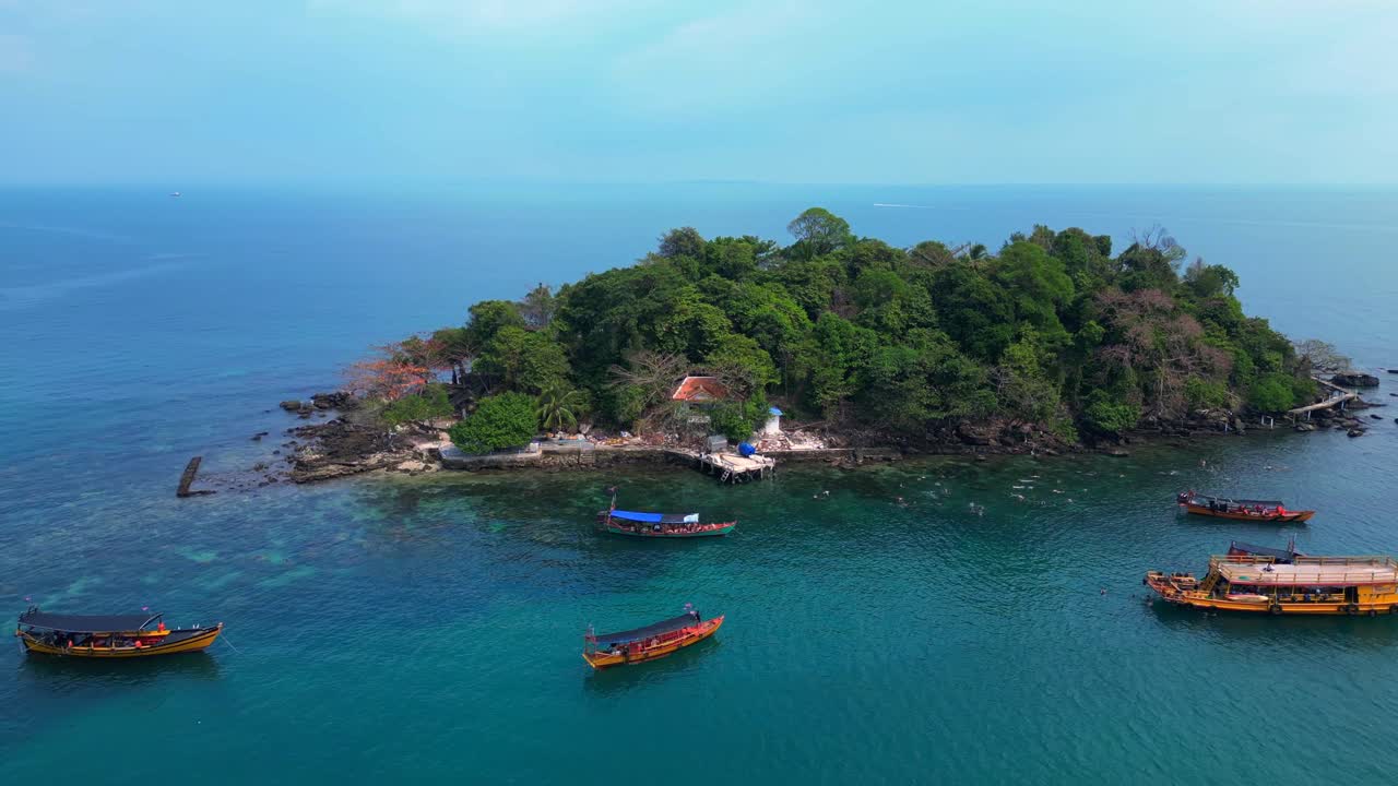 tourist boats surrounding a small tropical island in Koh Rong, Cambodia, with crystal clear water and lush vegetation. Lovely aerial view flight wide orbit overview drone