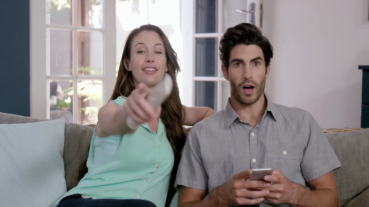 pareja feliz viendo televisión y usando un teléfono inteligente