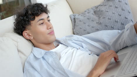relaxing on couch, teenage boy using laptop and raising hand in comfortable home setting