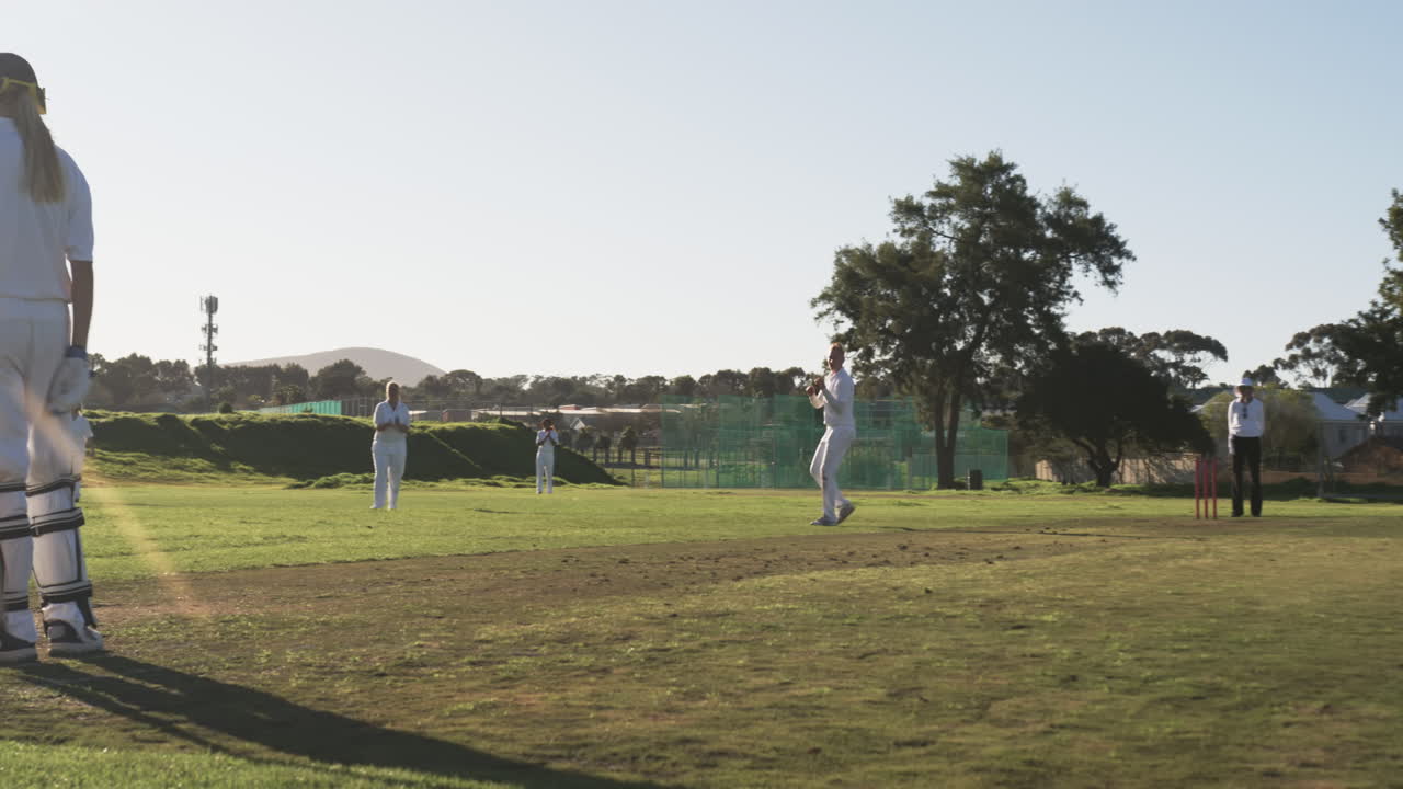 Playing cricket on sunny day, female players in white uniforms on field