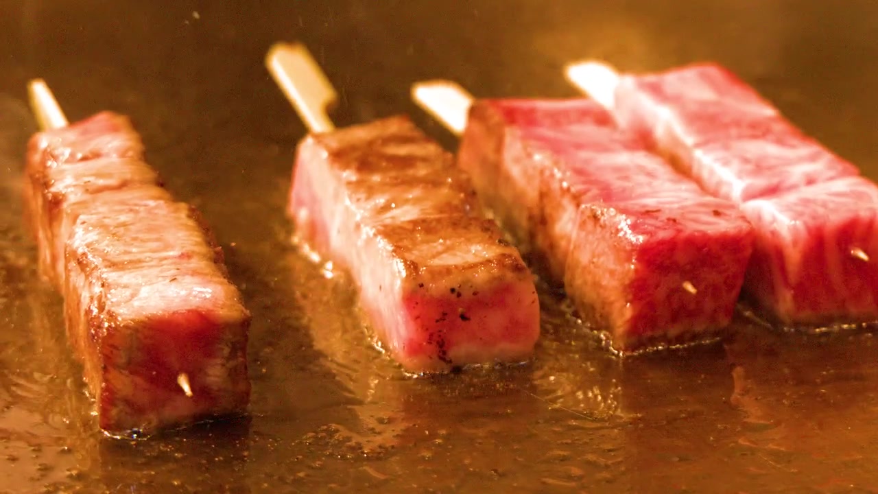 Spiedini di manzo Wagyu marmorizzato sfrigolano su una piastra teppanyaki calda in un primo piano