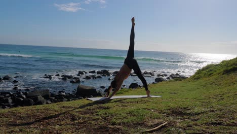 Eine-Schlanke-Frau,-Die-Yoga-Am-Burleigh-Beach-Praktiziert---Dreibeiniger-Herabhängender-Hund-Zur-Schlafenden-Taubenpose---Qld,-Australien---Weite-Zeitlupenaufnahme